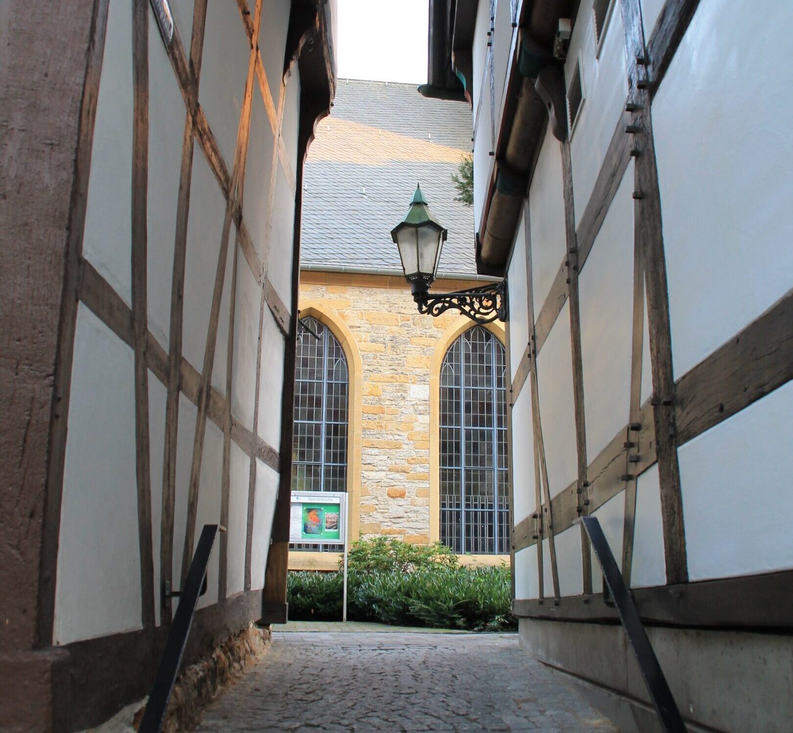 Schmaler Gang zwischen zwei Fachwerkhäusern. am Ende des Ganges ist ein kleiner Teil der Apostelkirche zu sehen.