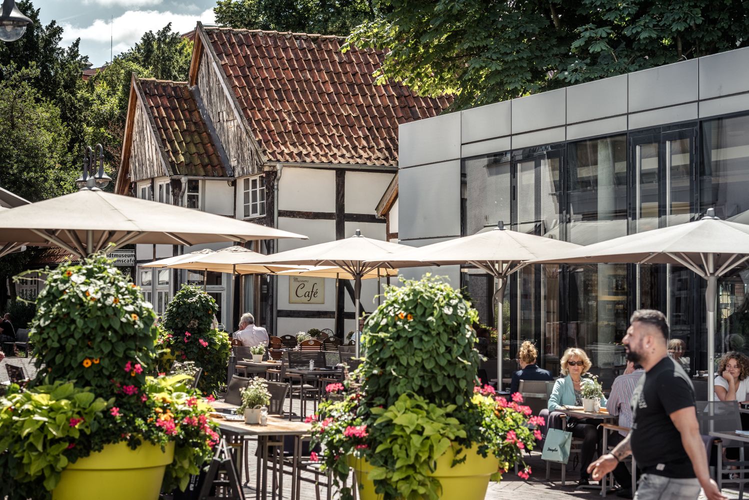 Außengastronomie am Kolbeplatz in Gütersloh. Einige Tische und Sonnenschirm sowie große Pflanzkübel vor dem Bankery und dem Café des Stadtmuseums Gütersloh