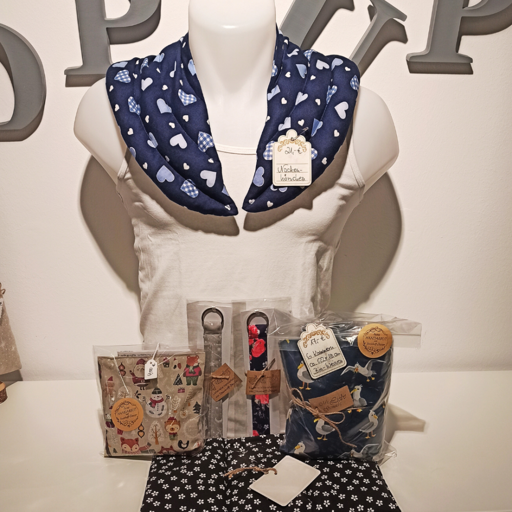 Ein Schaufensterpuppe mit um den Nackem gelegtem Körnerkissen, davor Körnerkissen in verschiedneen Größen sowie Schlüsselbänder.