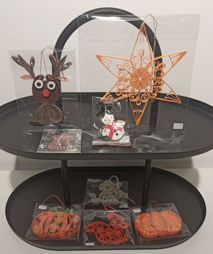 Acht Quilling-Dekorations-Artikel mit herbstlichen oder weihnachtlichen Motiven wie Kürbissen und Rentieren auf einer schwarzen Etagere