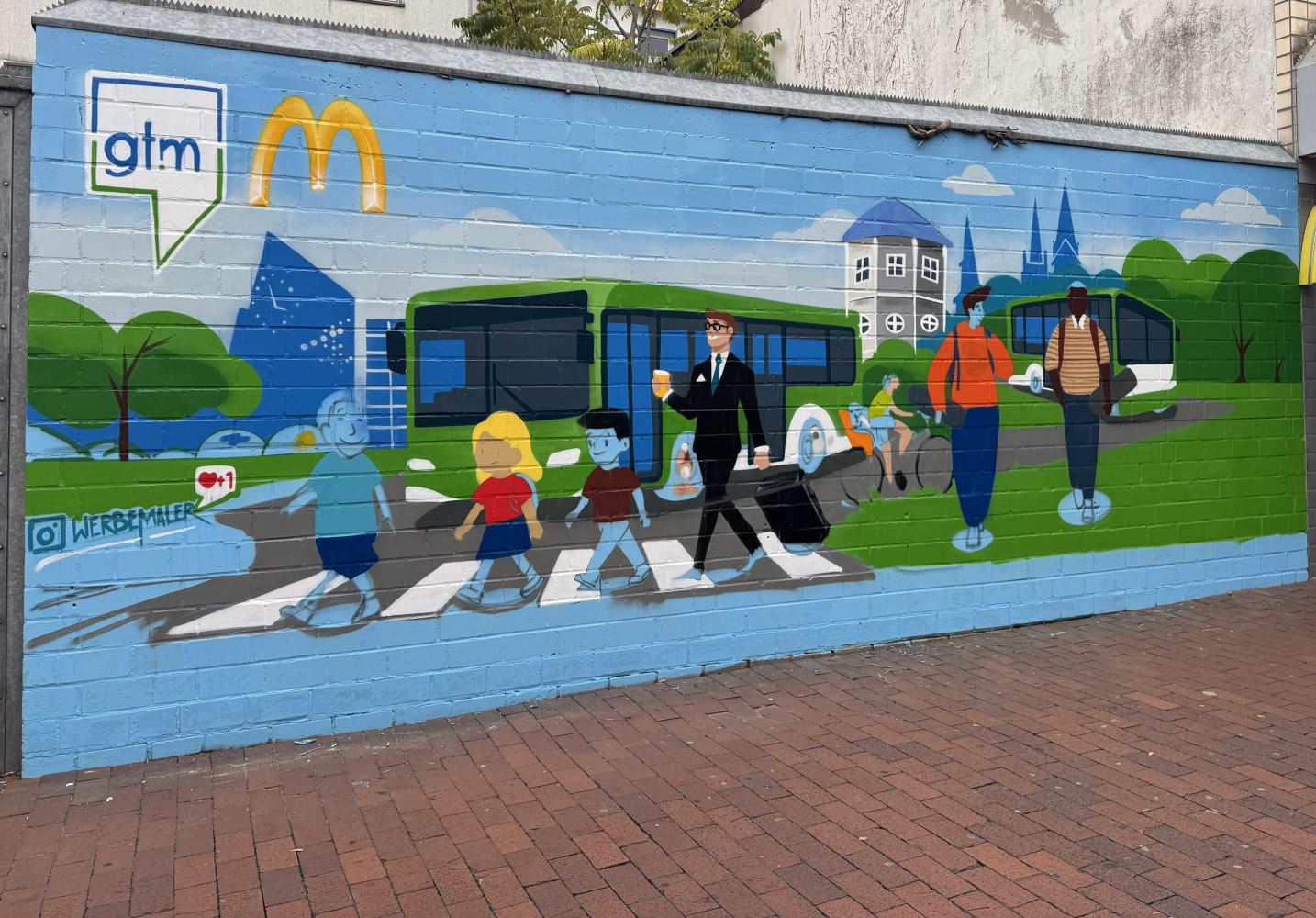 Wandgemälde mit mehreren Comicfiguren, Bussen und Radfahrenden. Oben in der linken Ecke das Logo von Gütersloh Marketing und McDonald's