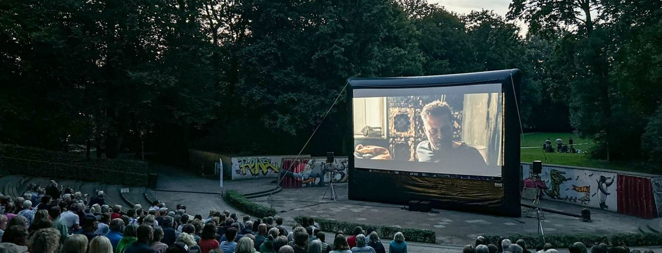 Freiluftkino-Event (Open Air Kino 2024-9348) Menschen sitzen auf einer Treppe und schauen einen Film im Freiluftkino